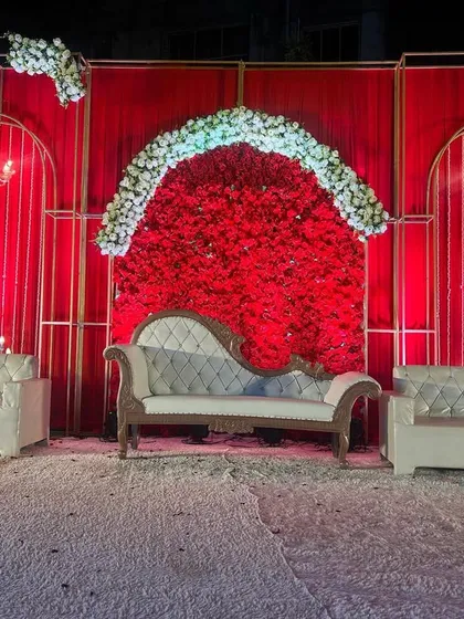 A centered shot of the all-red wedding stage, focusing on the main seating area. The symmetrical design with the central floral arch makes for a perfect photo backdrop.