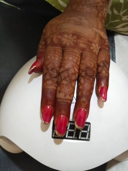 A bold and beautiful bridal look. These are gel extensions with a vibrant red gel polish and a sparkling gold glitter gradient on the tips. This style looks stunning against traditional henna designs.