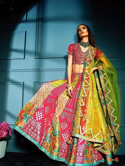 A full-length shot of a model in a vibrant, multi-colored lehenga. The dramatic studio lighting and powerful pose highlight the outfit's intricate patterns and bold colors, making it a standout piece for any ethnic wear portfolio.