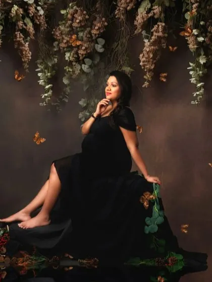 A dark and moody portrait of a mom-to-be in a black gown, seated in an enchanted forest setting.