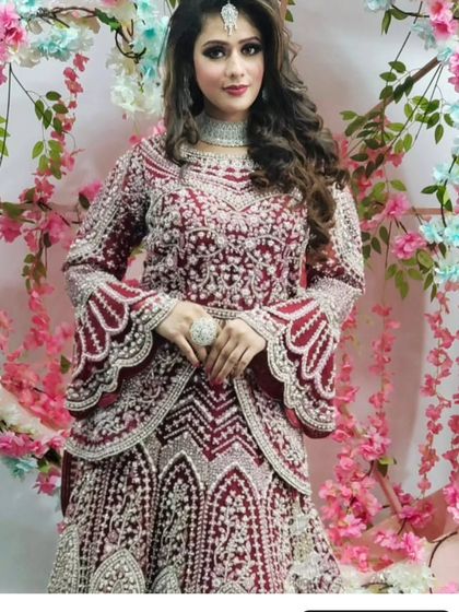 A model wearing a modern maroon gown with intricate silver and pearl embroidery and dramatic bell sleeves. This is a perfect outfit for a reception or cocktail event.