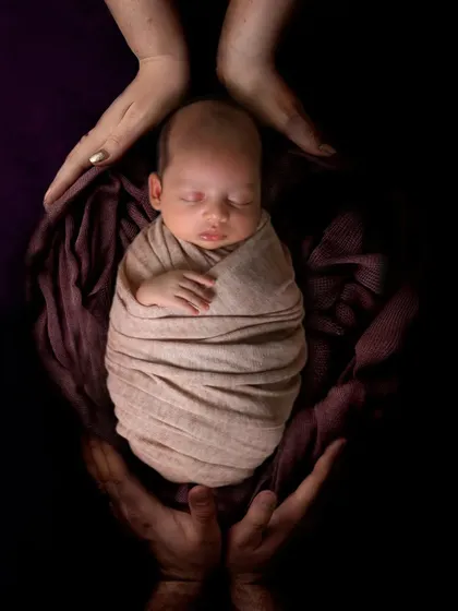 A powerful photo showing a swaddled newborn held securely in the hands of their parents.