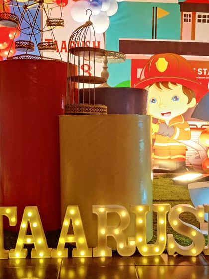 A close-up of a Fireman-themed setup, showing the 'TAARUSH' marquee letters and themed dessert plinths.