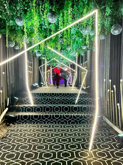 We guide your guests through a mesmerizing geometric tunnel of light for a truly modern and glamorous Sangeet entrance. This immersive walkway, featuring a custom patterned carpet and hanging greenery, sets a sophisticated and high-energy tone for the evening.