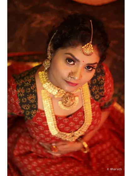A dramatic top-down portrait of a model in a traditional red lehenga. The warm, focused lighting creates a regal and intense mood.
