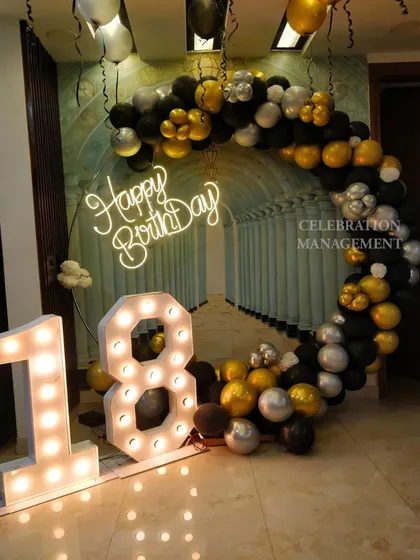 An 18th birthday is a huge milestone, and this setup makes a bold statement. A circular arch of black, silver, and gold balloons frames the large, illuminated '18' marquee numbers.