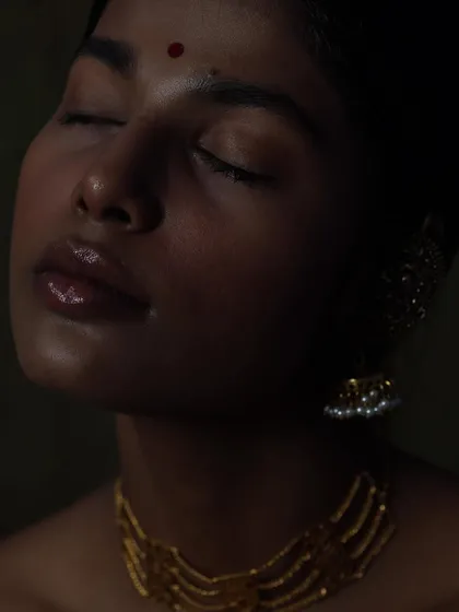 A dramatic close-up where the light just kisses the model's lips and cheek, drawing attention to the texture of the skin and the gleam of the gold.