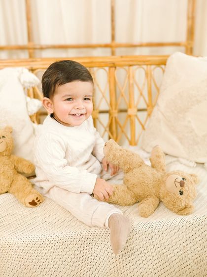 A sweet, direct-to-camera smile during a sitter session. The baby's happy expression and the warm, neutral tones of the set create a timeless and heartwarming portrait.