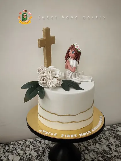 A simple and elegant all-white communion cake. The design features a praying girl figurine, a golden cross, and delicate white sugar roses. Sometimes, the most beautiful statements are the most understated.