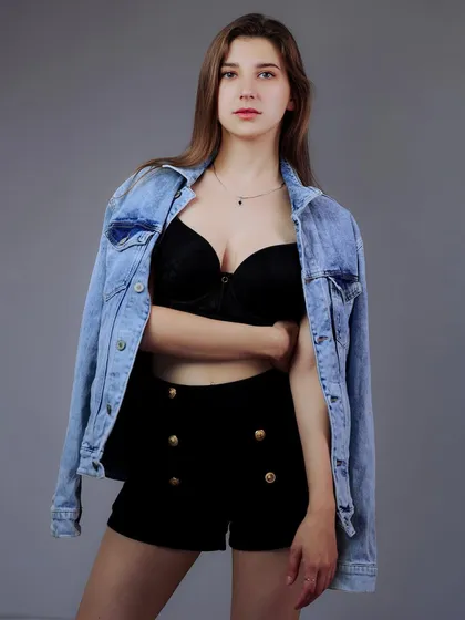 A classic model portfolio shot with a denim jacket over a black top against a solid grey background.