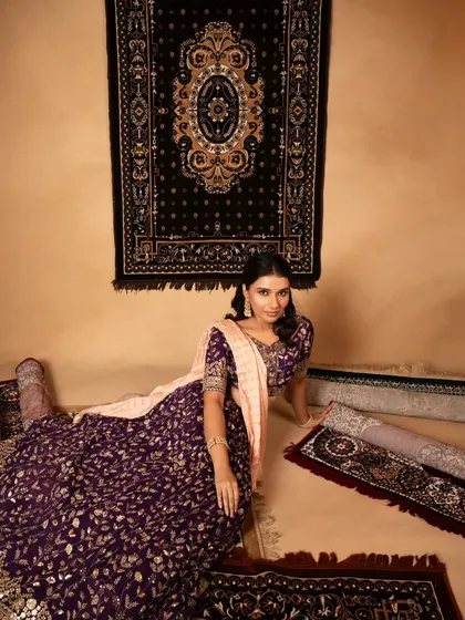 An artistic lookbook image where the model is seated amongst rolled carpets, which complement the colors in her lehenga. This creative setup elevates a standard commercial shoot.