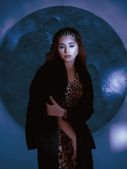 A moody, cinematic portrait using a single, focused light source. The blue tones and the moon-like prop in the background create a mysterious, nocturnal atmosphere.