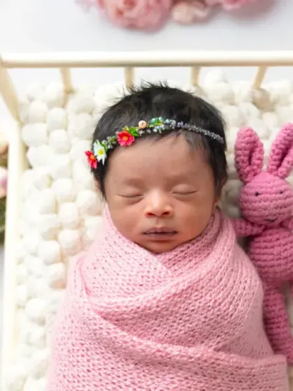 Sleeping soundly in a miniature bed, this newborn is surrounded by soft pink flowers. These styled setups create beautiful, dreamy portraits.