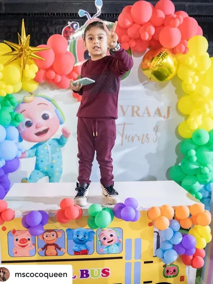 The birthday boy, Divraaj, looking stylish on his Cocomelon-themed stage. The backdrop features a school bus made of balloons, a signature element from the show.