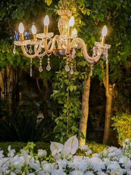 A crystal chandelier emerges from a bed of white flowers and greenery, a beautiful detail that merges nature with luxury.