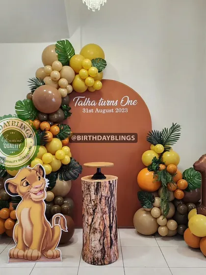 This clean and elegant Lion King first birthday setup features a simple terracotta-colored backdrop. A single Simba cutout, a tree-stump plinth, and a number '1' foil balloon create a focused and stylish photo corner.