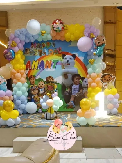A Cocomelon first birthday stage setup with a custom photo backdrop, pastel balloon arch, and character cutouts.