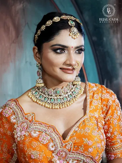 A bride glowing in a vibrant orange lehenga. The makeup features dramatic, smoky eyes and a neutral lip, creating a stunning contrast that is both bold and beautiful.
