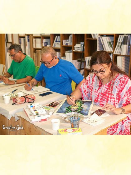 A group of adult students sits at a table, deeply focused on their watercolor paintings, demonstrating the calm and concentration that art brings.