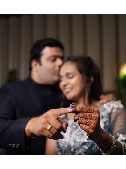 A creative focus on the engagement ring, with the couple sharing a sweet kiss in the background.