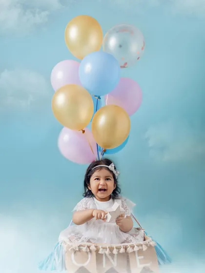 Up, up, and away for her first birthday. This 'hot air balloon' setup with pastel balloons against a dreamy blue sky creates a whimsical and happy portrait. I love designing creative themes for baby milestone photoshoots.