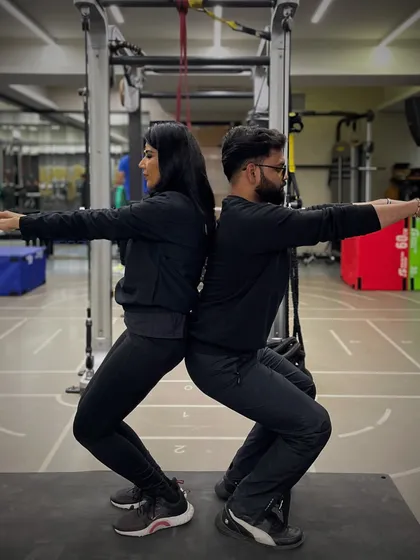 Partner workouts help with form and motivation. Here, a couple works on posture and squat depth together, providing support and accountability.