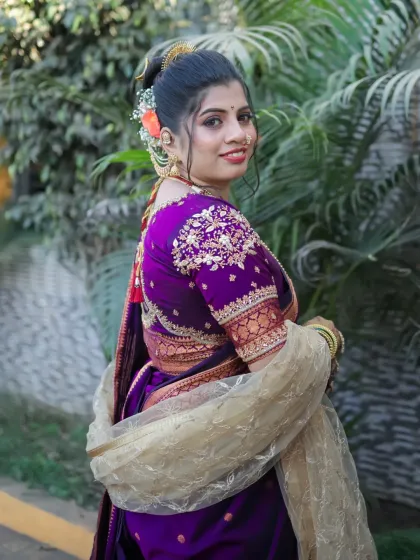 A side profile showing the elegant bridal bun adorned with fresh flowers and the beautiful details of her purple Paithani saree.