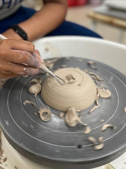 After throwing a piece, the next step is trimming. This student is using a tool to carve away excess clay and define the foot of their bowl.