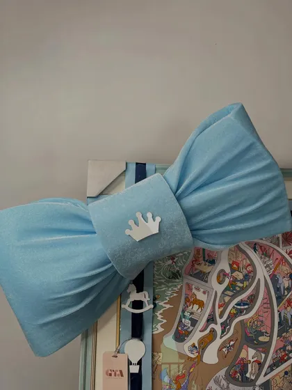 A close-up of the custom-made blue bow, featuring a small crown emblem, adding a regal touch to this storybook-style art piece.