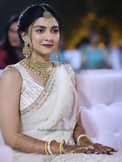 A candid shot of the bride during her ring ceremony. Her makeup features a bold lip and defined eyes, paired with a classic updo and maang tikka.