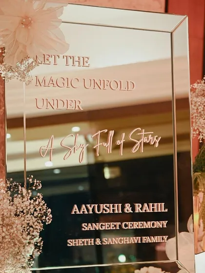 A mirrored welcome sign for a sangeet, with the message "Let the magic unfold under a sky full of stars."