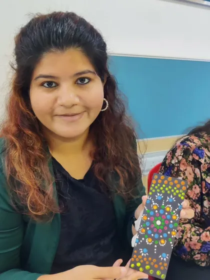 A close-up of a participant from the corporate workshop with her finished dot mandala bookmark. Her pleased expression reflects the satisfaction of creating something beautiful in a short amount of time.