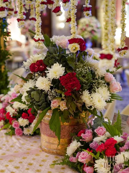 A close-up of a floral centerpiece in a rustic gold vase. The mix of red, pink, and white flowers with fresh greenery creates a classic and beautiful arrangement.