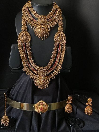 A magnificent antique-finish bridal set with two layered necklaces. The detailed choker and long haaram are both adorned with deity figures, perfect for achieving that classic South Indian bride look.