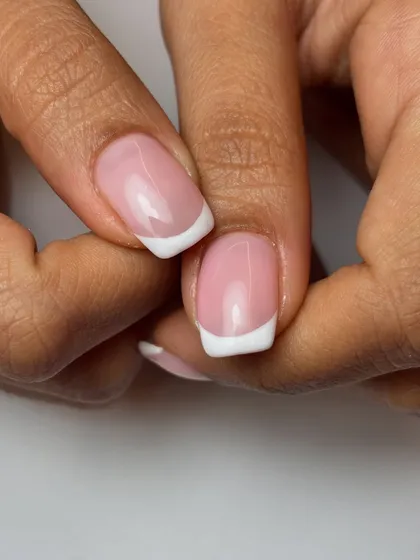 A close-up of a classic French manicure on short, square-shaped nails. This timeless look is all about precision and a clean, healthy-looking finish.