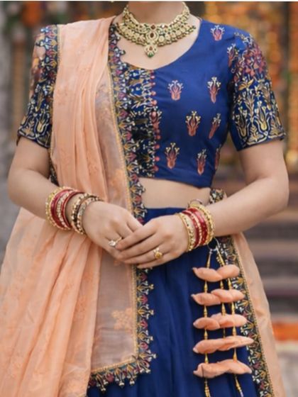 A close-up of the blouse and accessories, showing the colorful embroidery and the traditional red and gold bangles.