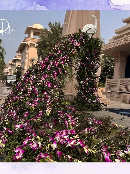 A majestic peacock installation for a welcome lunch. The peacock's tail is a cascading arrangement of purple orchids and green foliage, creating a stunning and unique entrance piece.