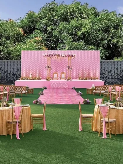 The Vidhi Mandap for the pastel lawn wedding. The stage features a quilted pink backdrop and delicate floral arrangements, creating a soft and romantic focus point for the ceremony.