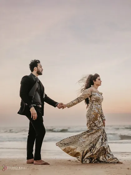 A dramatic and stylish shot on a Goa beach at sunset. The wind in her hair and the elegant evening wear create a powerful and cinematic pre-wedding portrait.