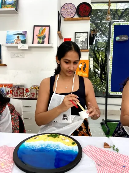 A participant carefully works on her resin beach art, adding details to the shoreline.