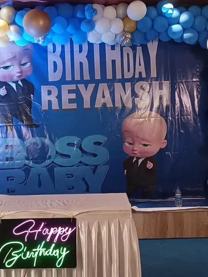 A classic Boss Baby themed birthday party, with a large character backdrop, blue and white balloon columns, and a neon "Happy Birthday" sign.