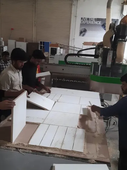 The CNC router has completed its cutting path, and students are now carefully removing the individual parts from the spoilboard.