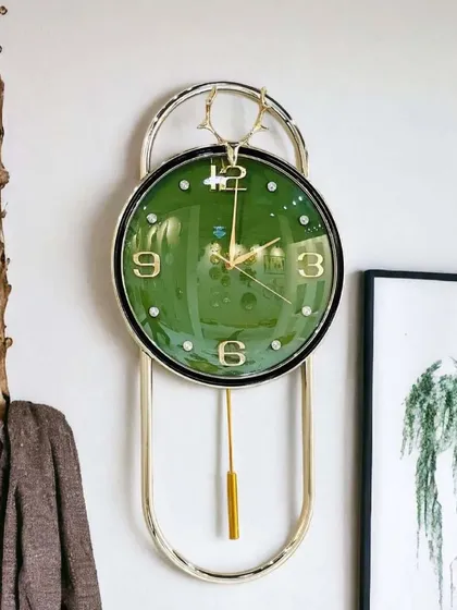 This imported wall clock features a rich green face with classic gold numerals and a deer-head crest. The elegant pendulum design and polished metal frame make it a sophisticated choice for both modern and traditional interiors.