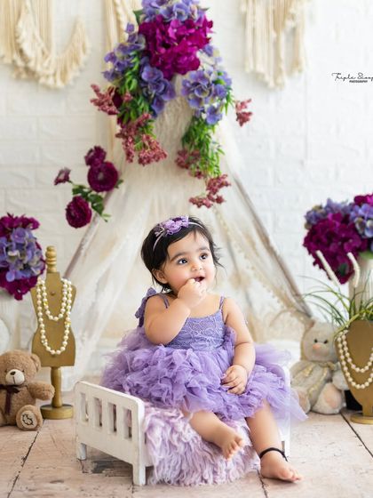 A thoughtful moment from a baby girl in a lovely purple dress. The boho-chic setup with a teepee and teddy bears creates a soft and dreamy atmosphere.