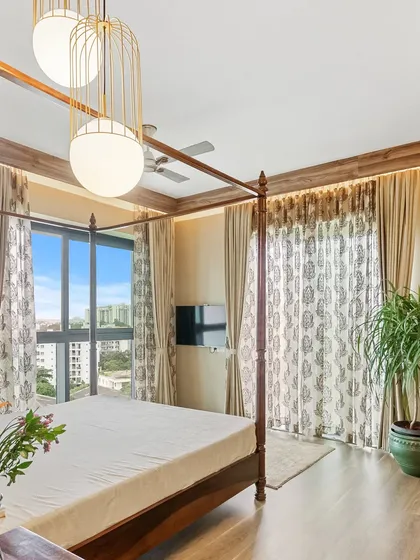 A master bedroom with a classic four-poster bed and large windows offering a city view. The elegant pendant lights and printed curtains add a touch of modern sophistication to the timeless furniture.