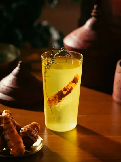 A bright yellow turmeric-infused drink. The fresh turmeric root is included as a prop to communicate the natural ingredients.