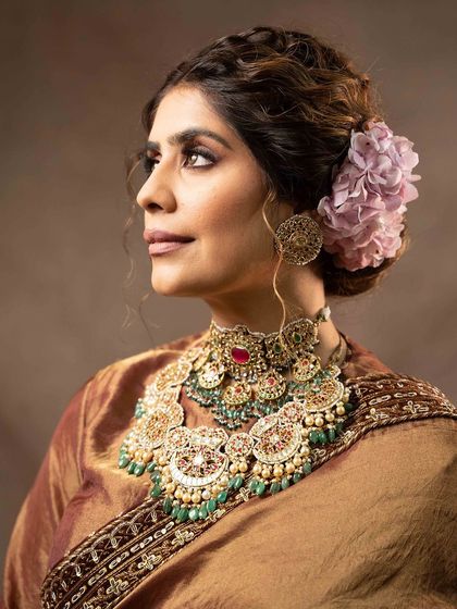A profile portrait highlighting the elaborate bridal jewelry and hairstyle. The flower in her hair and the detailed choker add to the traditional yet sophisticated aesthetic.