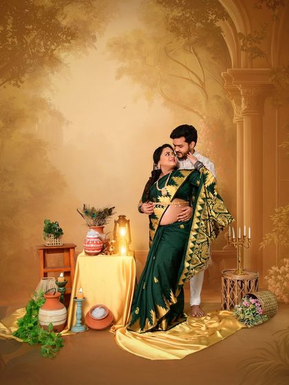 A romantic pose from a traditional maternity session. The couple, dressed in elegant ethnic wear, shares a loving gaze against a warm, painterly backdrop with classic Indian decor elements.