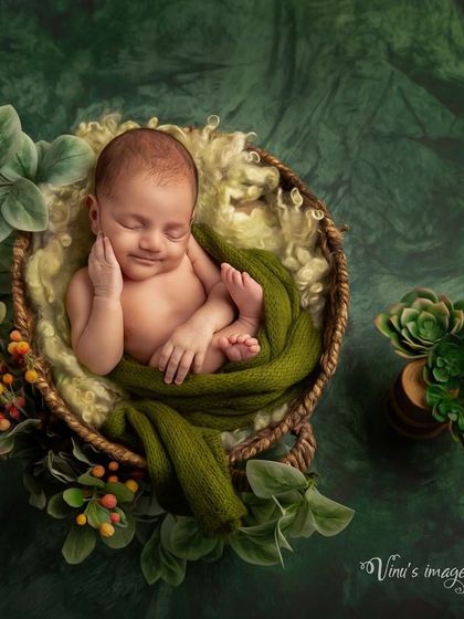 Green is a client favorite for its calming and natural feel. Here, a smiling baby is nestled in a basket, surrounded by different shades of green and leafy textures.