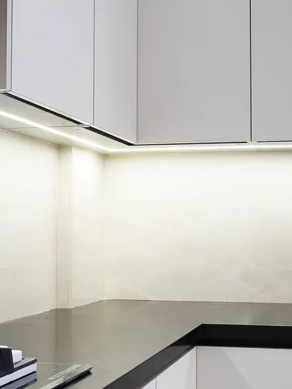 A detail shot showing the clean intersection of the white cabinets and the black countertop. The integrated LED strip lighting provides excellent task lighting while adding a layer of warmth to the minimalist design.